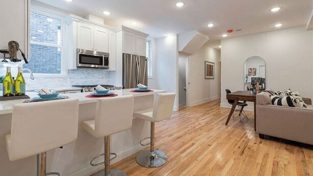 A modern kitchen with white cabinets, stainless steel appliances, and a bar area with white stools.