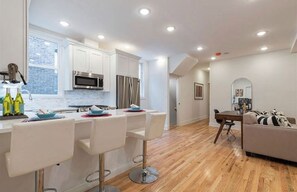 Una cocina moderna con armarios blancos, electrodomésticos de acero inoxidable y una barra con taburetes blancos.