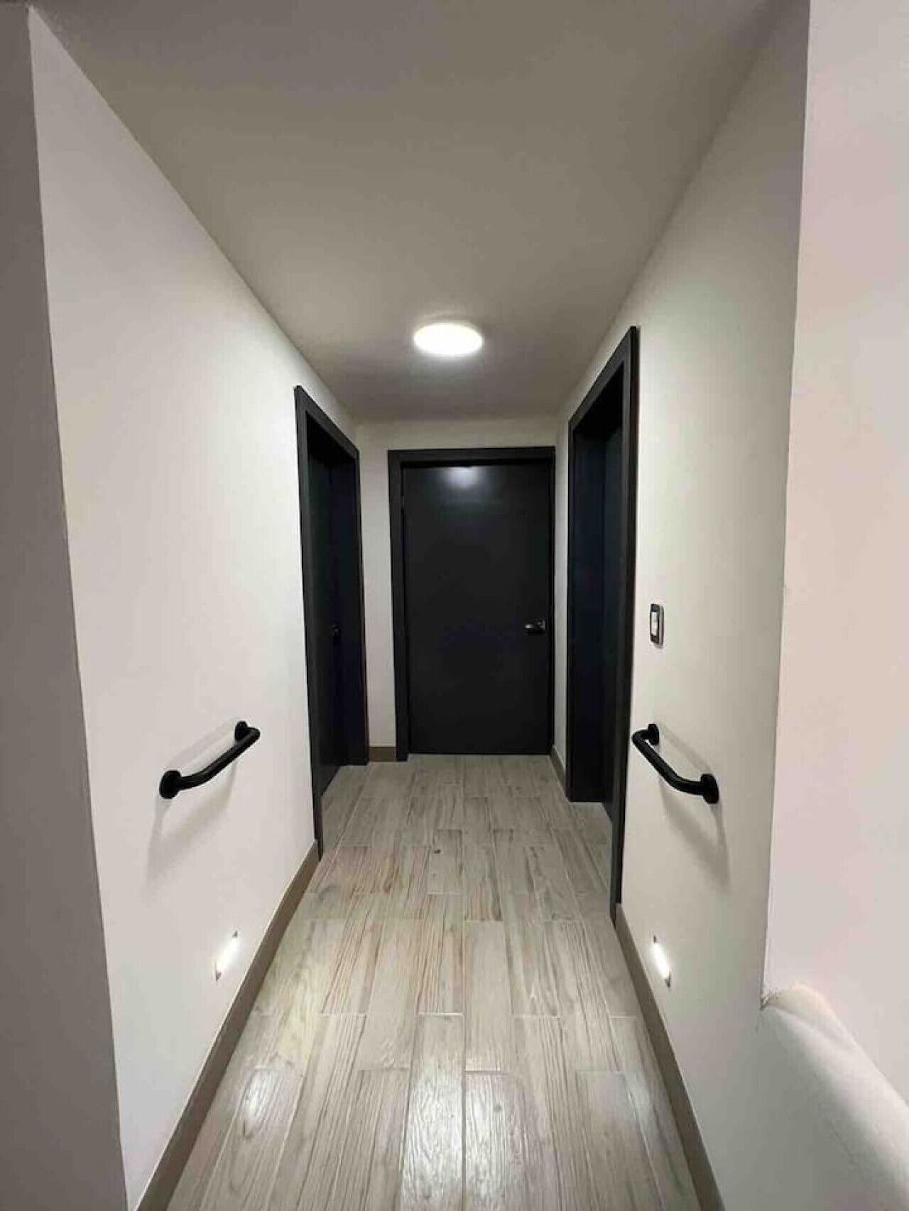 A narrow hallway with wooden flooring, white walls, and black doors.