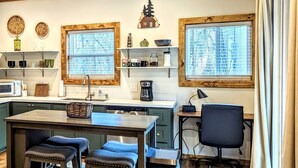 Een moderne keuken met houten plafond, een zithoek met krukken, een koffieapparaat en een zwarte bureaustoel.