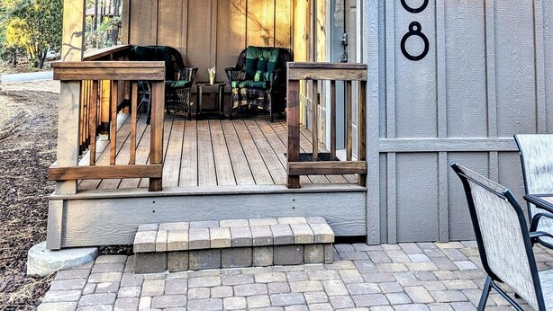 Een houten huisje met een veranda, een bordje met de tekst 'The Cozy Cottage' en het nummer '408' op de muur.