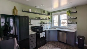 Cucina con frigorifero nero, piano cottura, lavello e pavimento in legno.