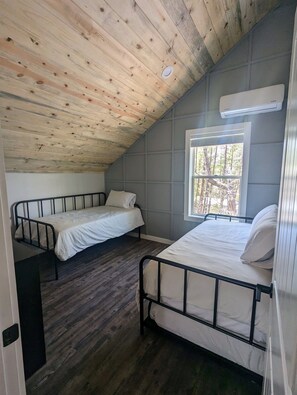 Une chambre avec deux lits, un plafond en bois et une fenêtre donnant sur la forêt.