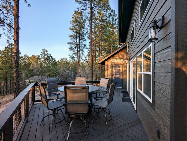 A wooden deck with outdoor furniture, a door labeled "The Porch," and a view of a forested area. - Pinetop Getaway w/ Sunset Deck & Fire Pit Table (Pinetop-Lakeside)