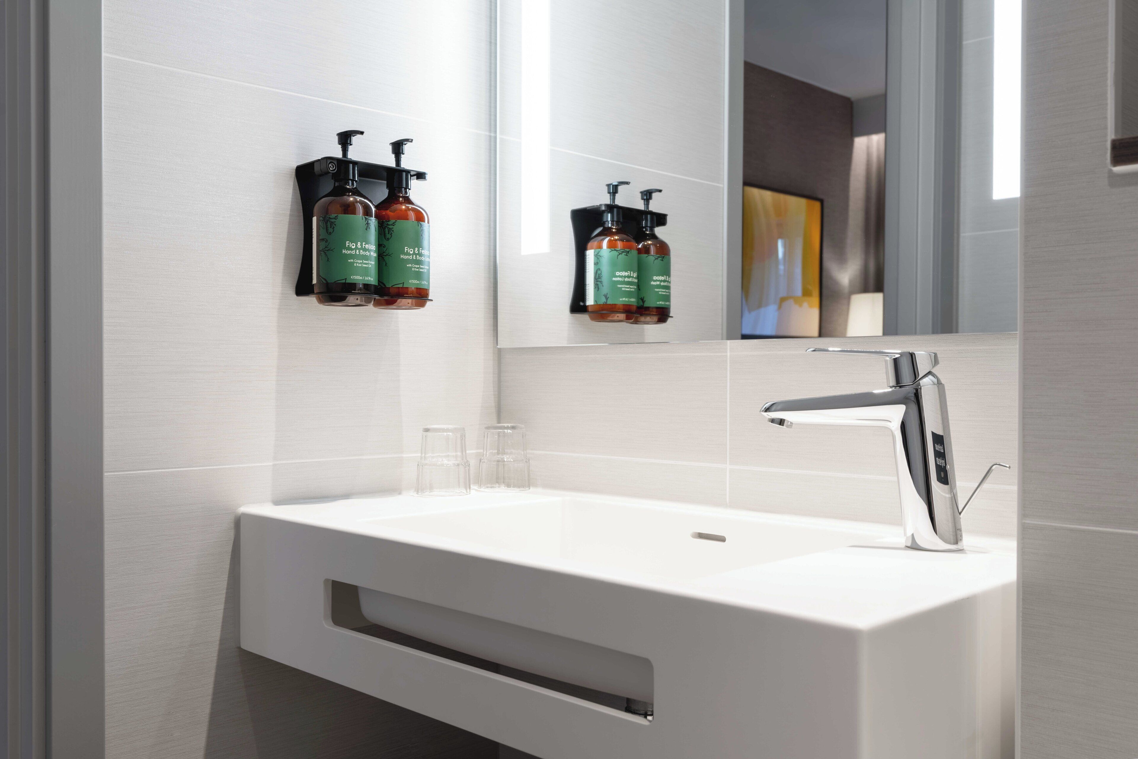 A modern bathroom with a white sink, a chrome faucet, and two green hand soap dispensers mounted on the wall.