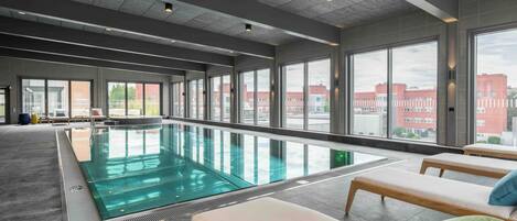 A modern indoor swimming pool with clear views of the cityscape through large windows.