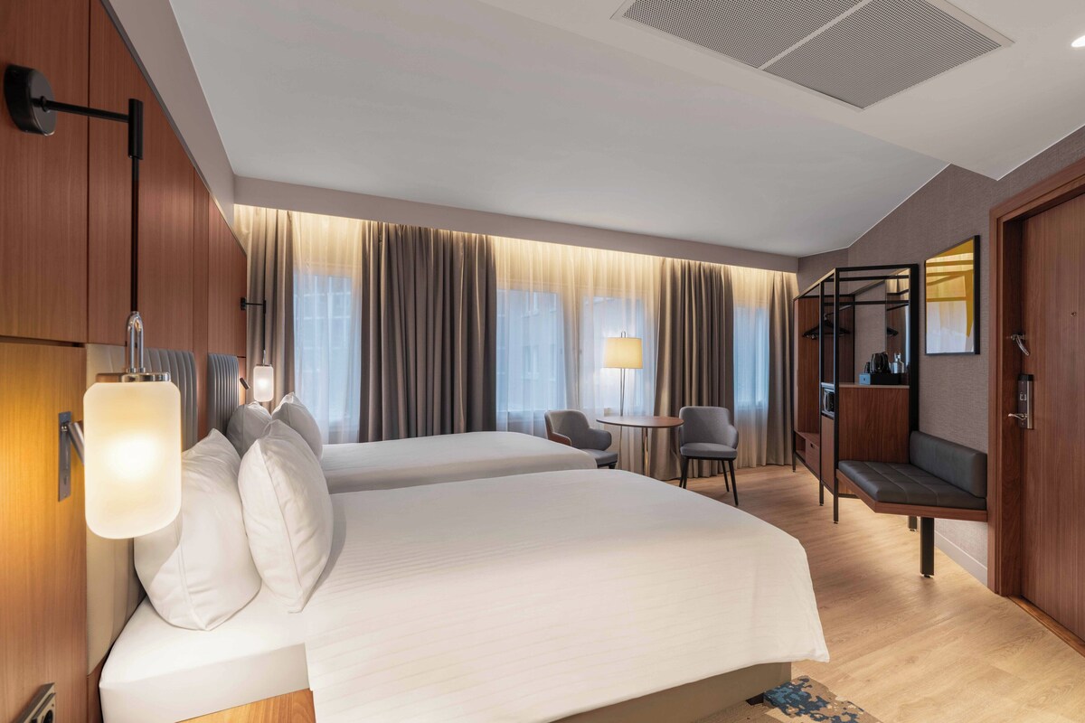 A modern hotel room with two beds, a seating area, and a small table.