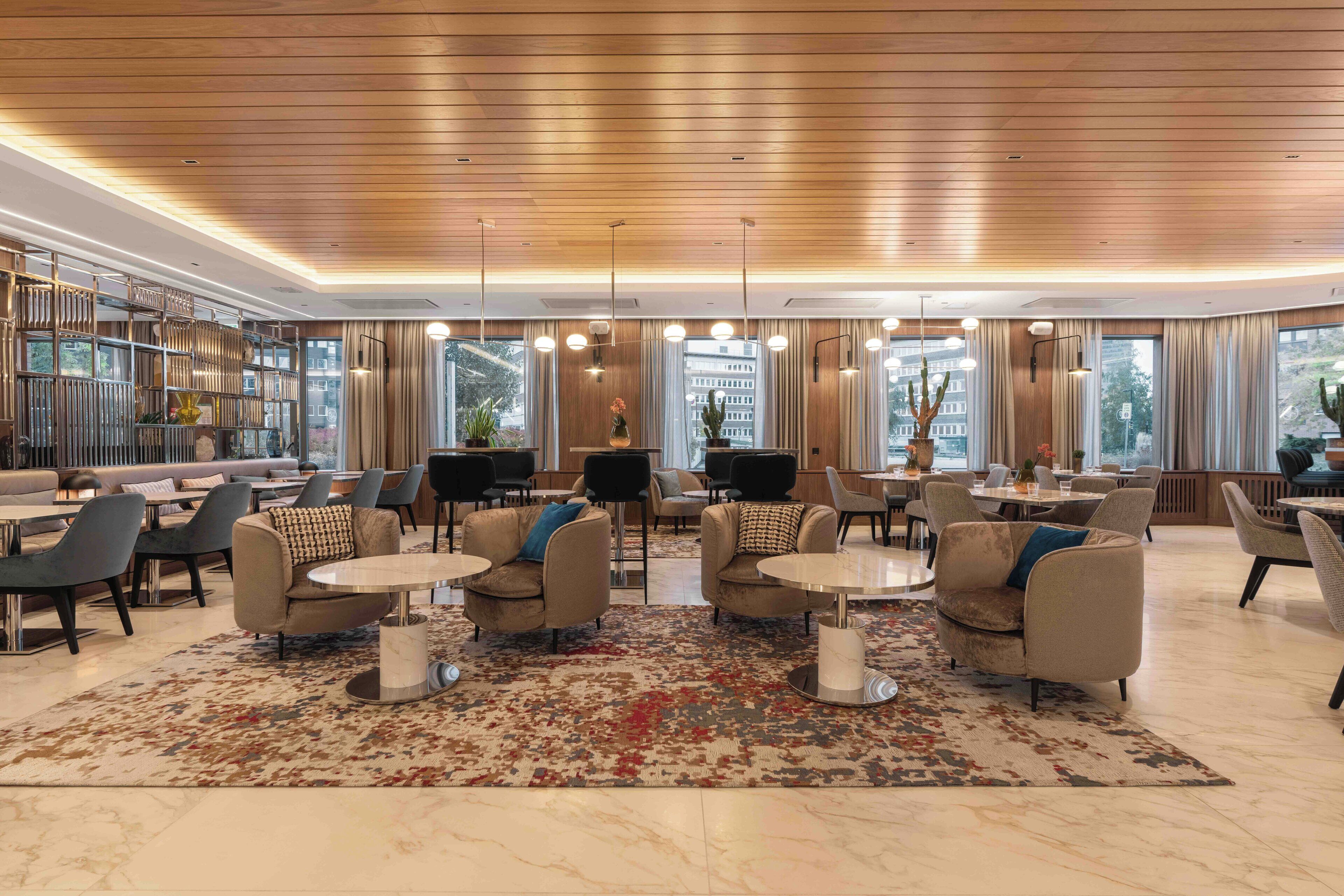 Eine geräumige Lobby mit modernen Möbeln, großen Fenstern und einer Holzzieldecke.
