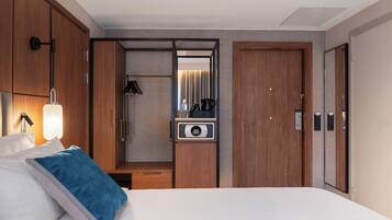 A modern hotel room with a large bed, a wardrobe, a mirror, and a minibar.
