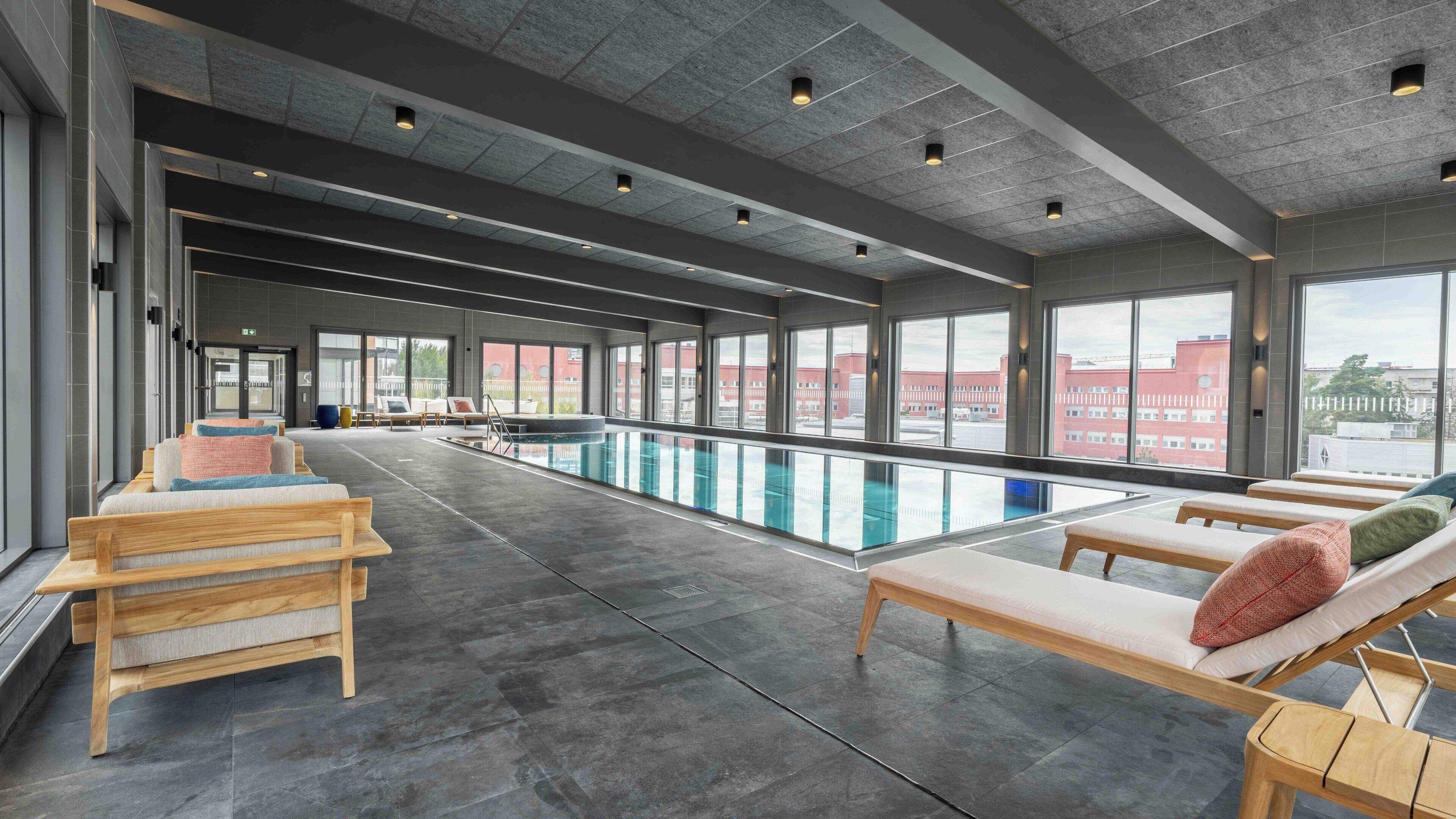 A modern indoor pool area with wooden loungers and a clear view of the outside.
