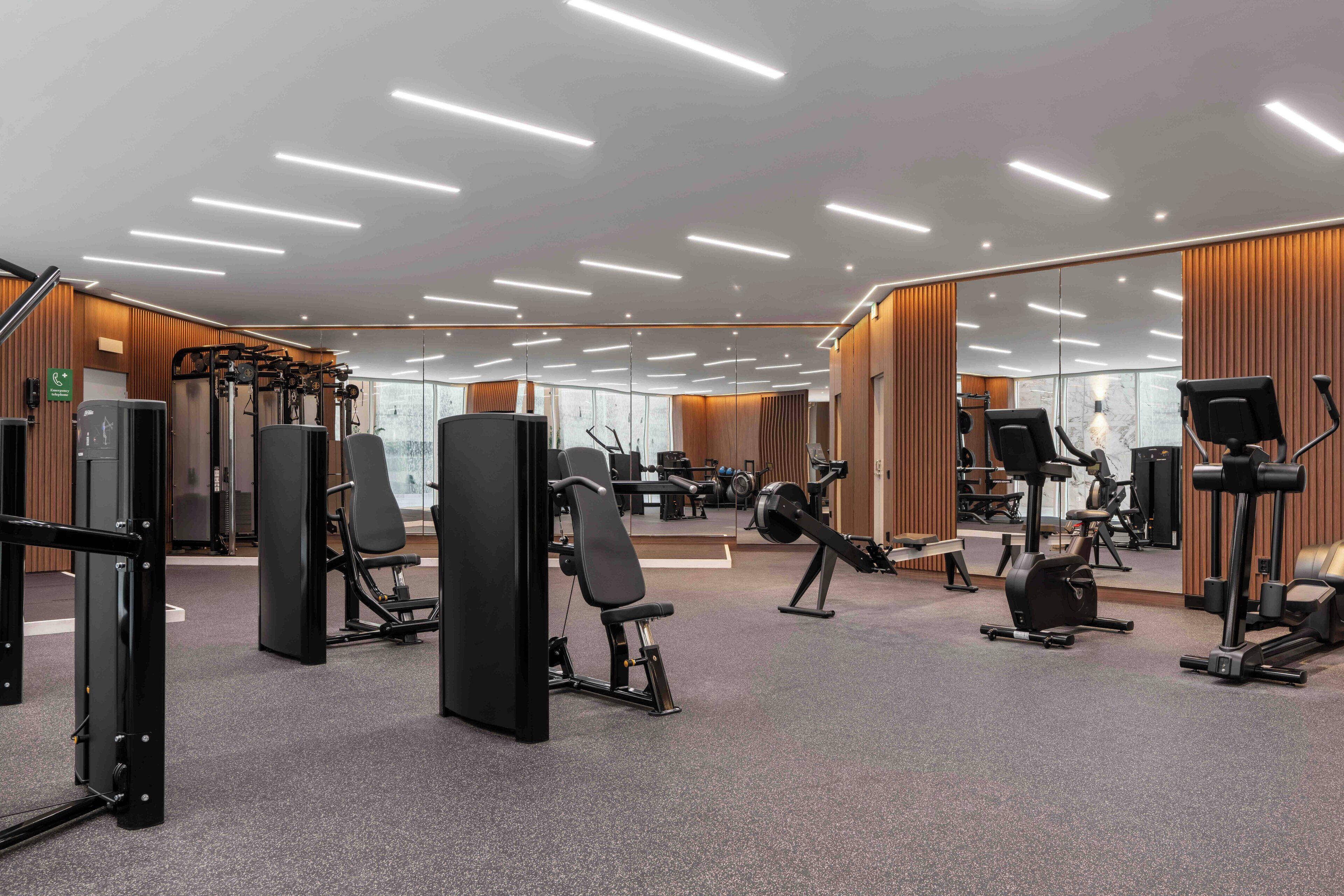 Un gimnasio moderno con diferentes equipos de ejercicio, paredes con espejos y un interior limpio y bien iluminado.
