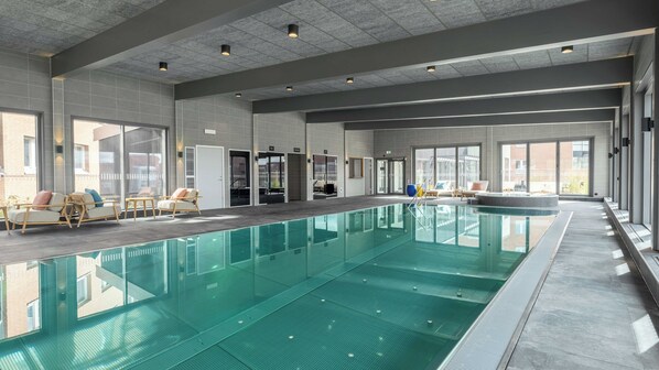 A large indoor swimming pool with clear water, surrounded by lounge chairs and a sunbed.