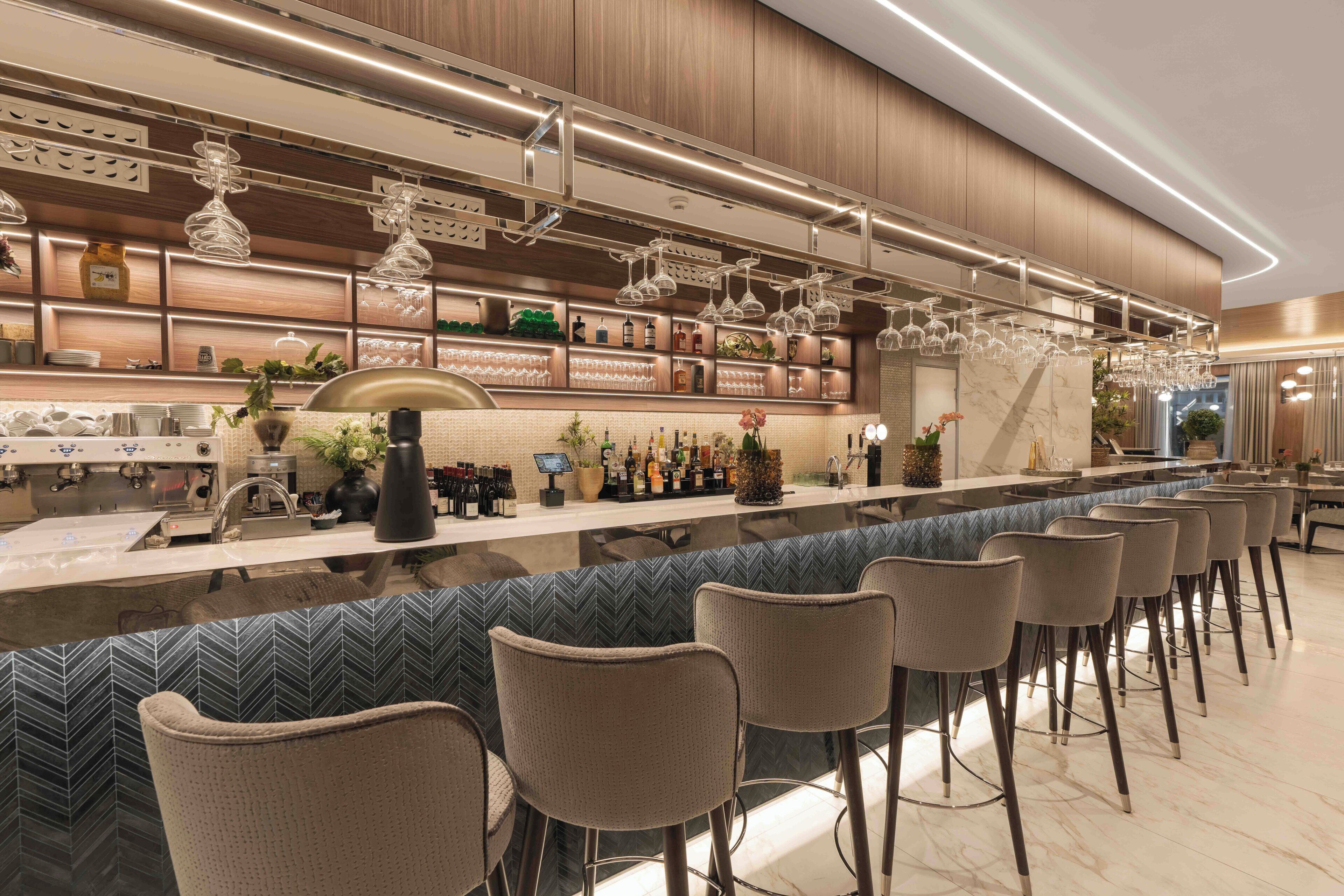 Un espace bar moderne doté d’un long comptoir, de tabourets et d’une variété de bouteilles et de verres.