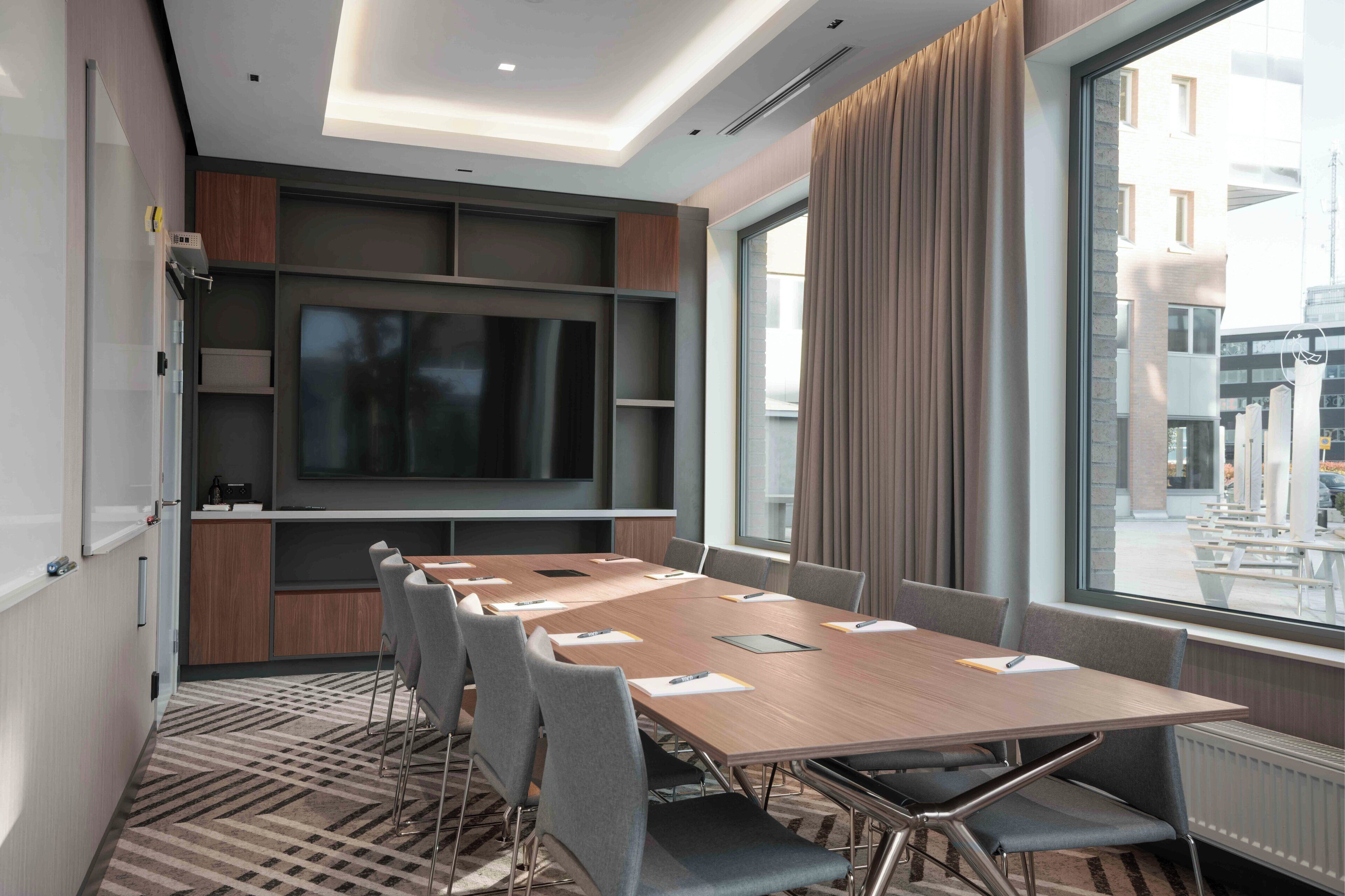 A conference room with a large table, chairs, a flat-screen TV, and a view of the city through large windows.