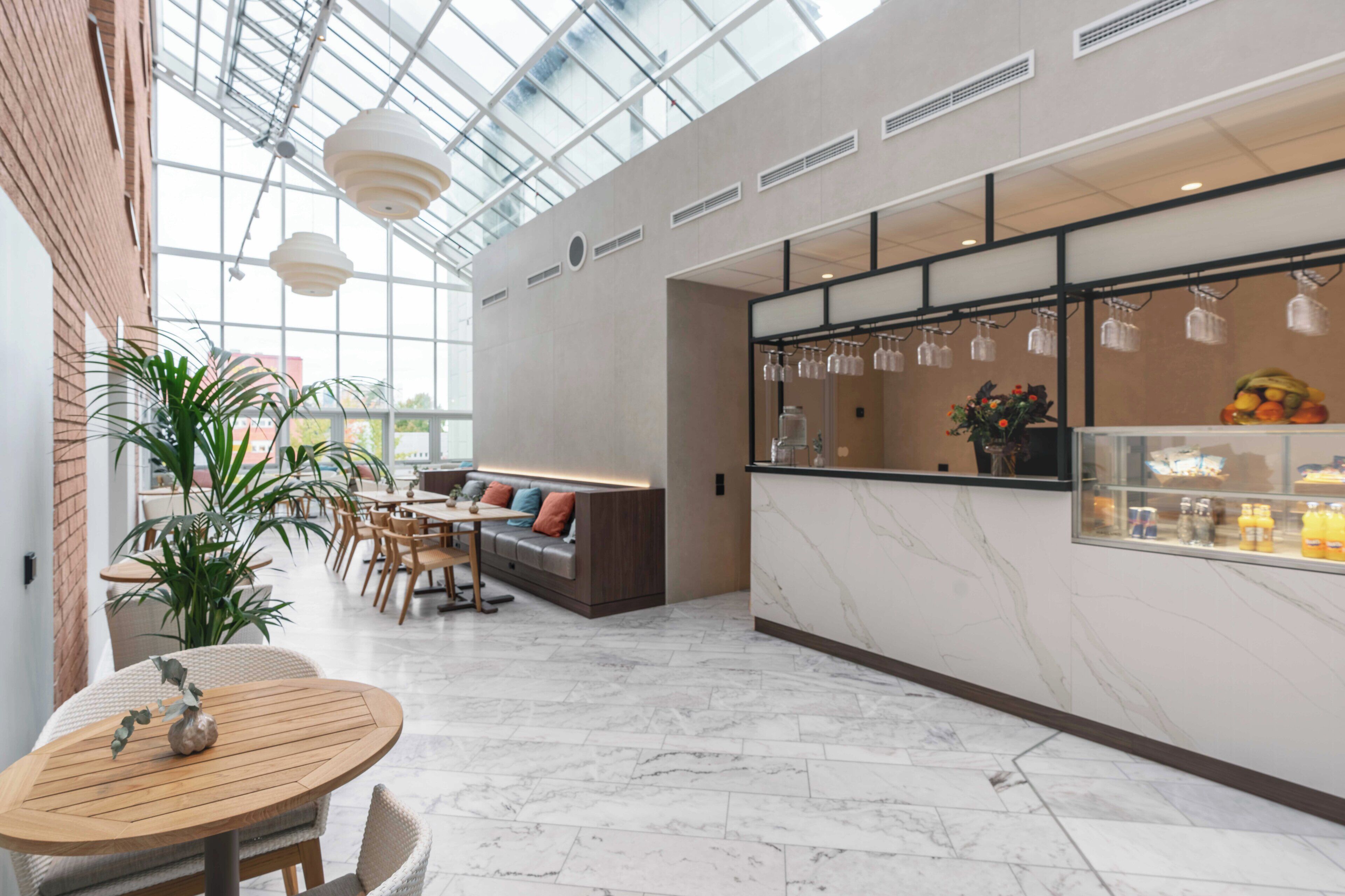 Un interior moderno con techo de vidrio, una zona de estar con sofá y sillones, una barra con una exposición de frutas y una planta en maceta.