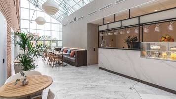 Un interior moderno con techo de vidrio, una zona de estar con sofá y sillones, una barra con una exposición de frutas y una planta en maceta.