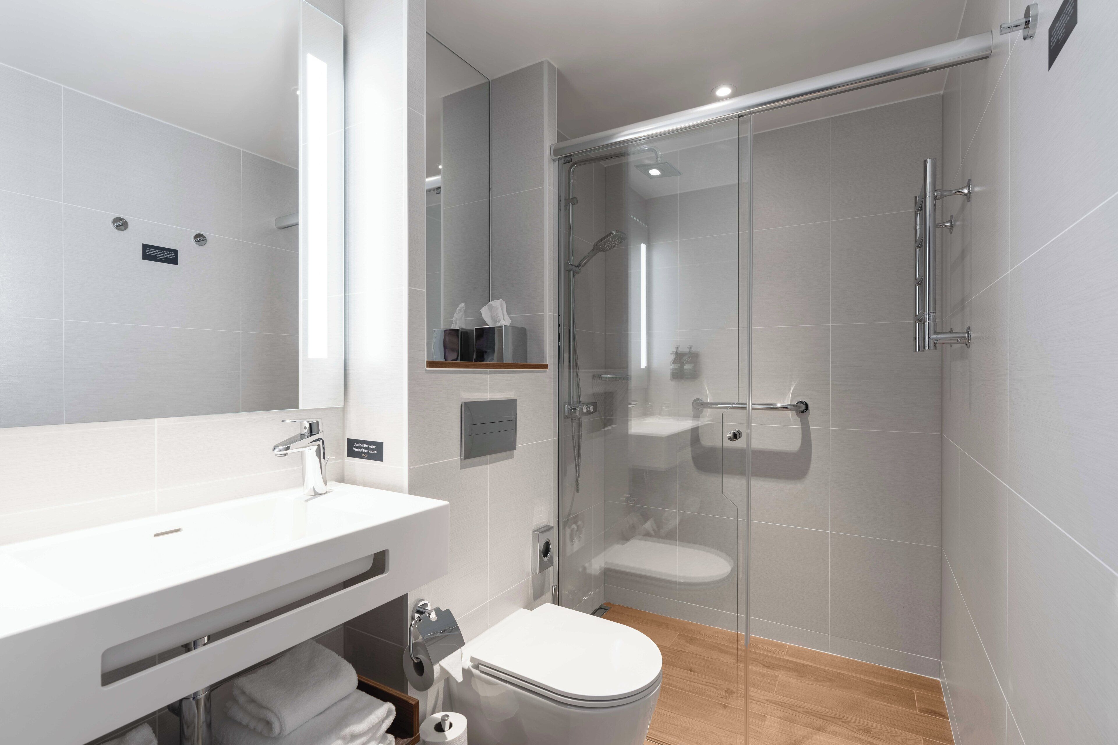 A modern bathroom with a glass-enclosed shower, a white sink, and a toilet.