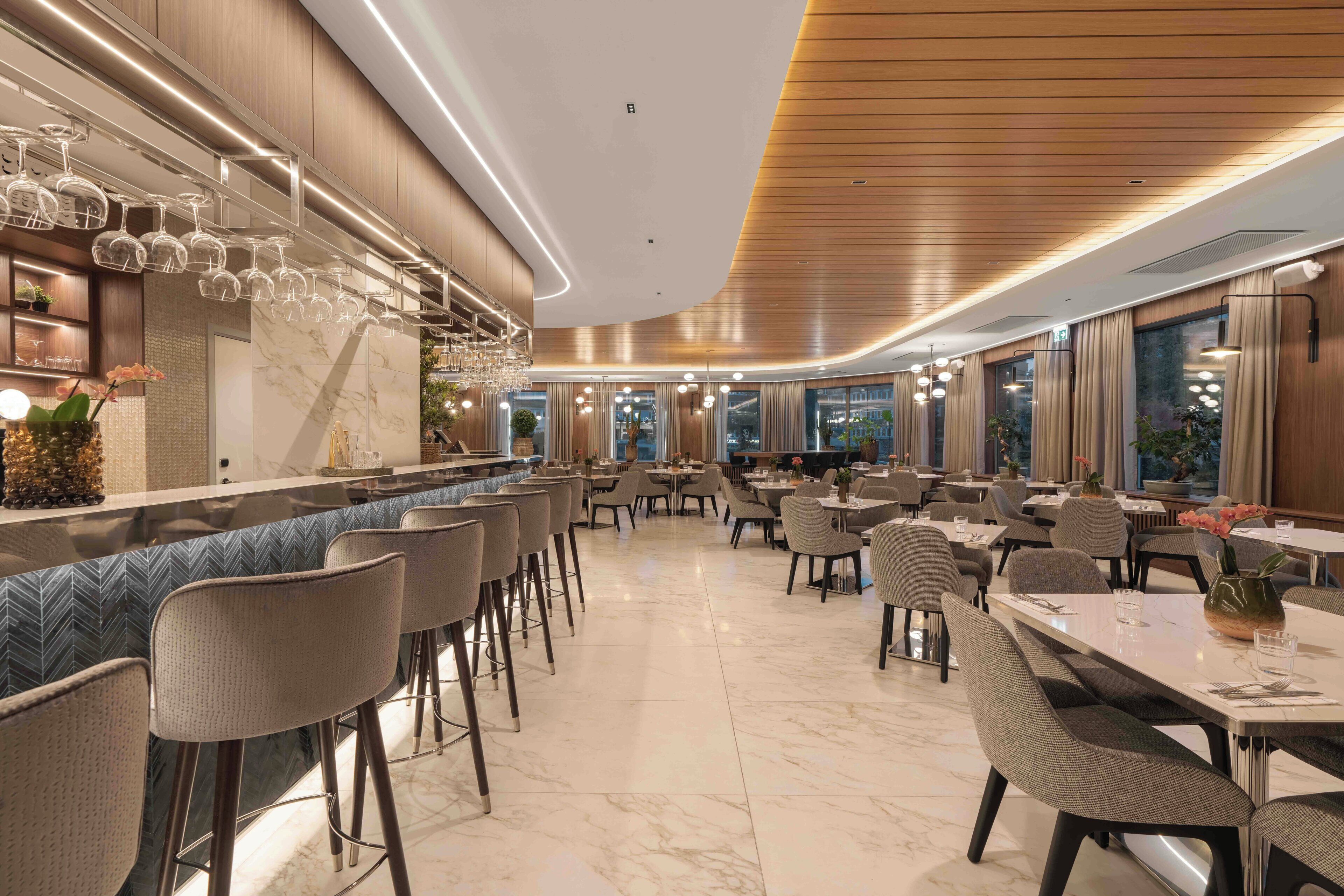 A modern restaurant with a bar area, marble flooring, and contemporary furniture.