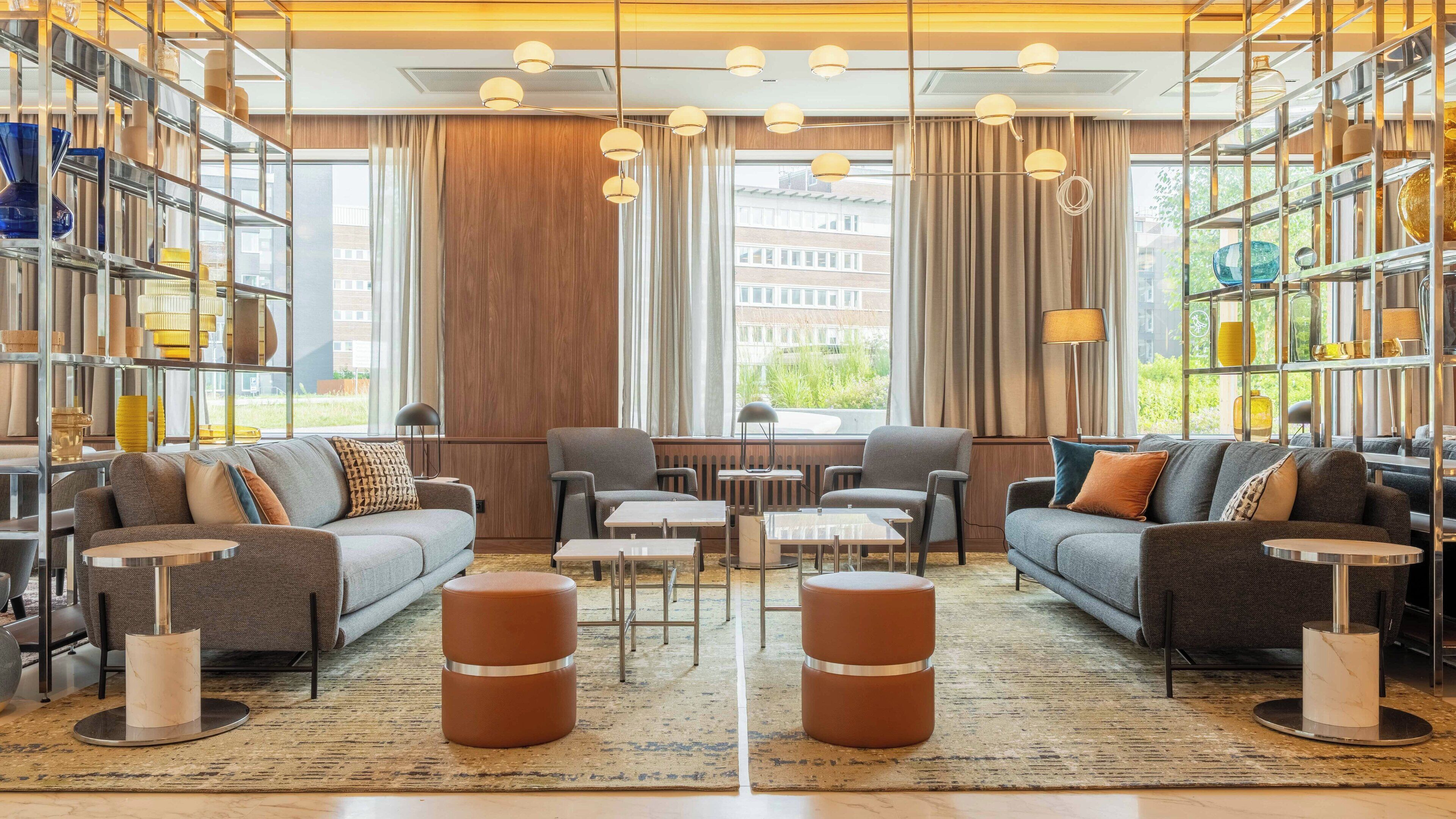 A modern hotel lobby with a central seating area, large windows, and a variety of decorative items on shelves.