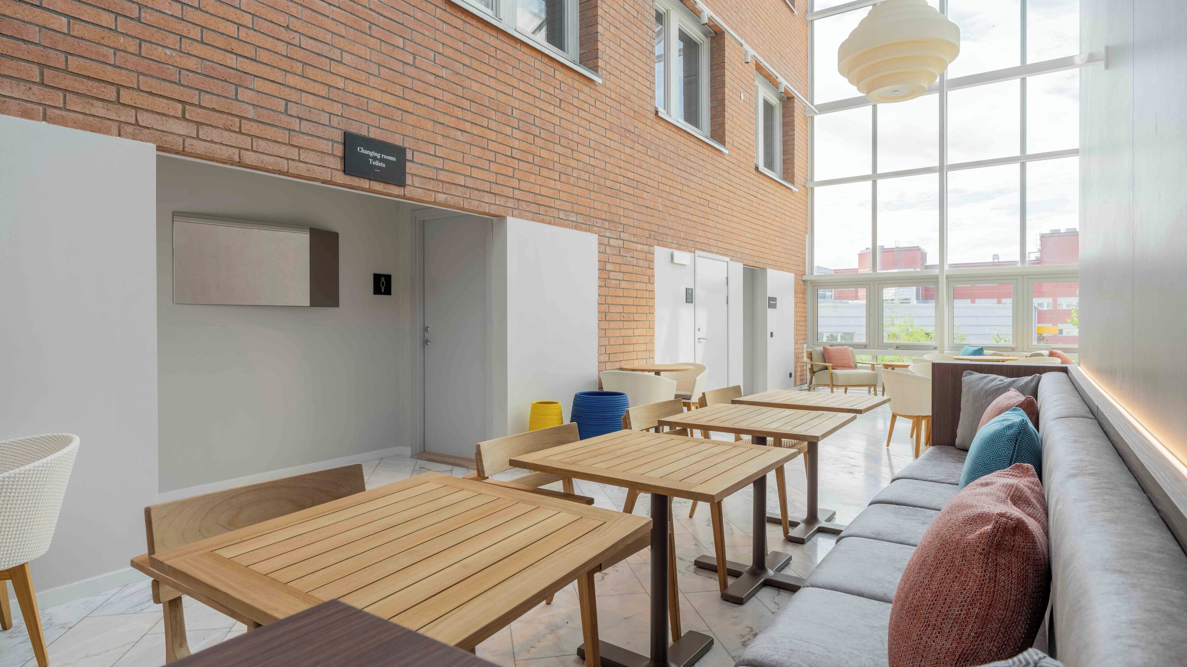 A modern communal area with wooden tables and chairs, a sofa, and a changing room sign.