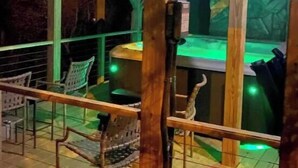 Une terrasse extérieure en bois, avec un coin bar, des chaises et un mur de pierre en arrière-plan.