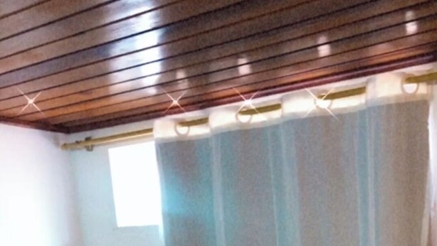 A hotel room with a neatly arranged bed, a window with curtains, and a wooden ceiling. - Flats Paraty (Patitiba Paraty)