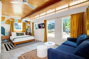 A modern bedroom with a bed, a blue sofa, a small table, and a ceiling fan. - Heated Pool • Sand V'ball • Mins>DT • Sleeps 10 (Austin)