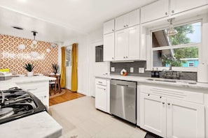 A modern kitchen with white cabinets, a stainless steel dishwasher, and a window overlooking the outside.