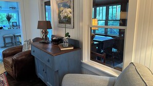 A cozy living room with a wooden cabinet, a sofa, a dining table, and a window with a view of the outdoors.