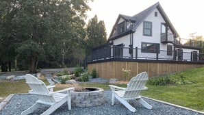 A house with a deck, two Adirondack chairs, and a stone fire pit.