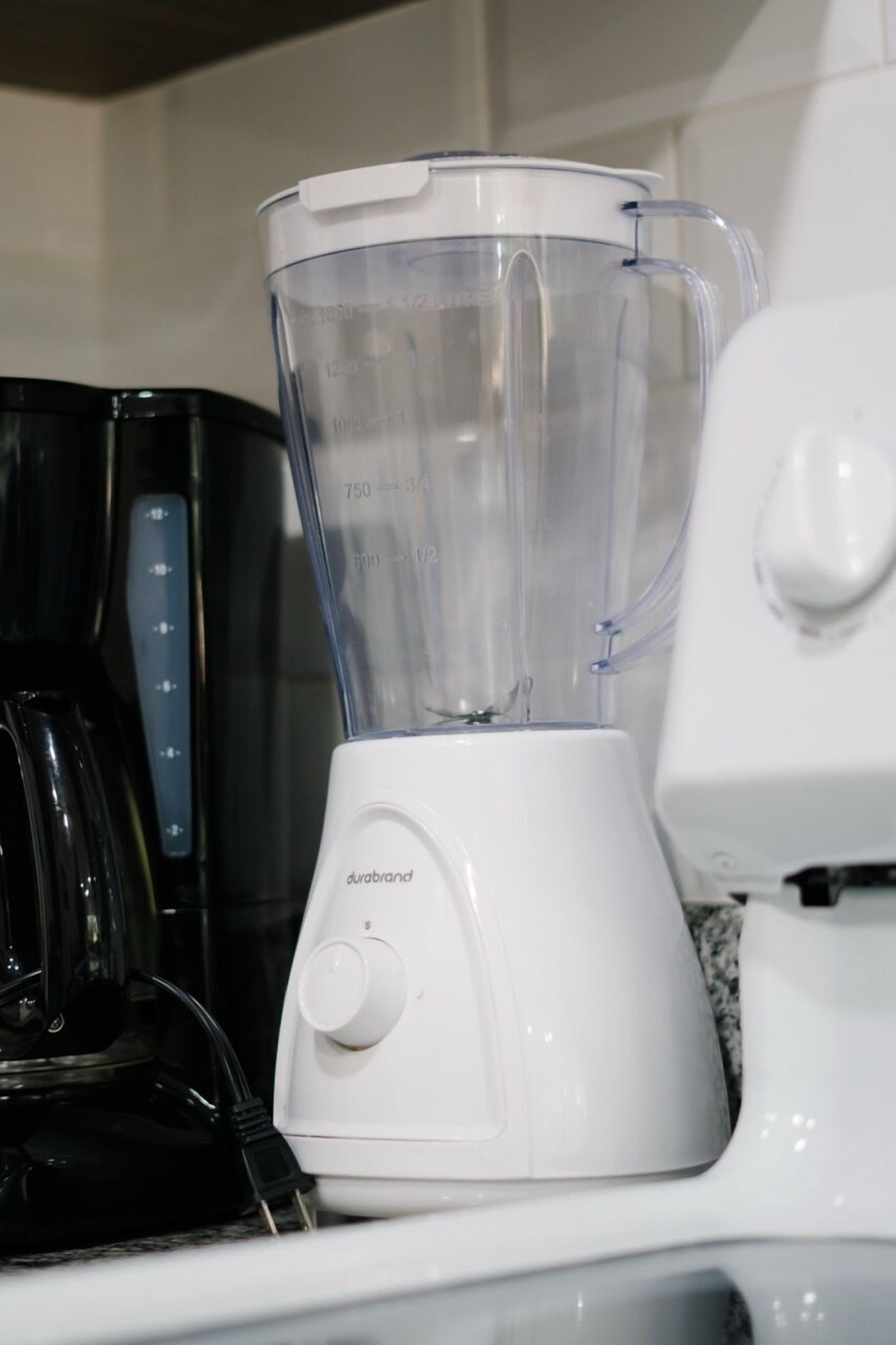 A white blender with measurement markings on the container, placed on a countertop next to a coffee maker.