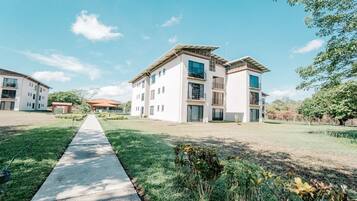 Un edificio residencial moderno con un camino central, rodeado de vegetación y otros edificios.