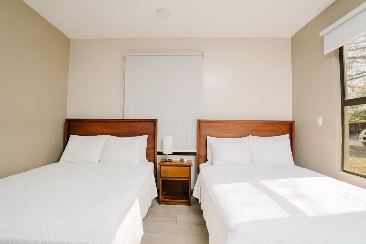 A hotel room with two beds, a nightstand, a window, and a view of the outside.