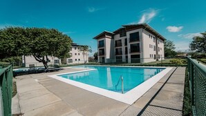 A swimming pool with a clear blue water, surrounded by a paved deck. In the background, there are two multi-story buildings with balconies. - Apartamento Ganesha Liberia (Liberia)