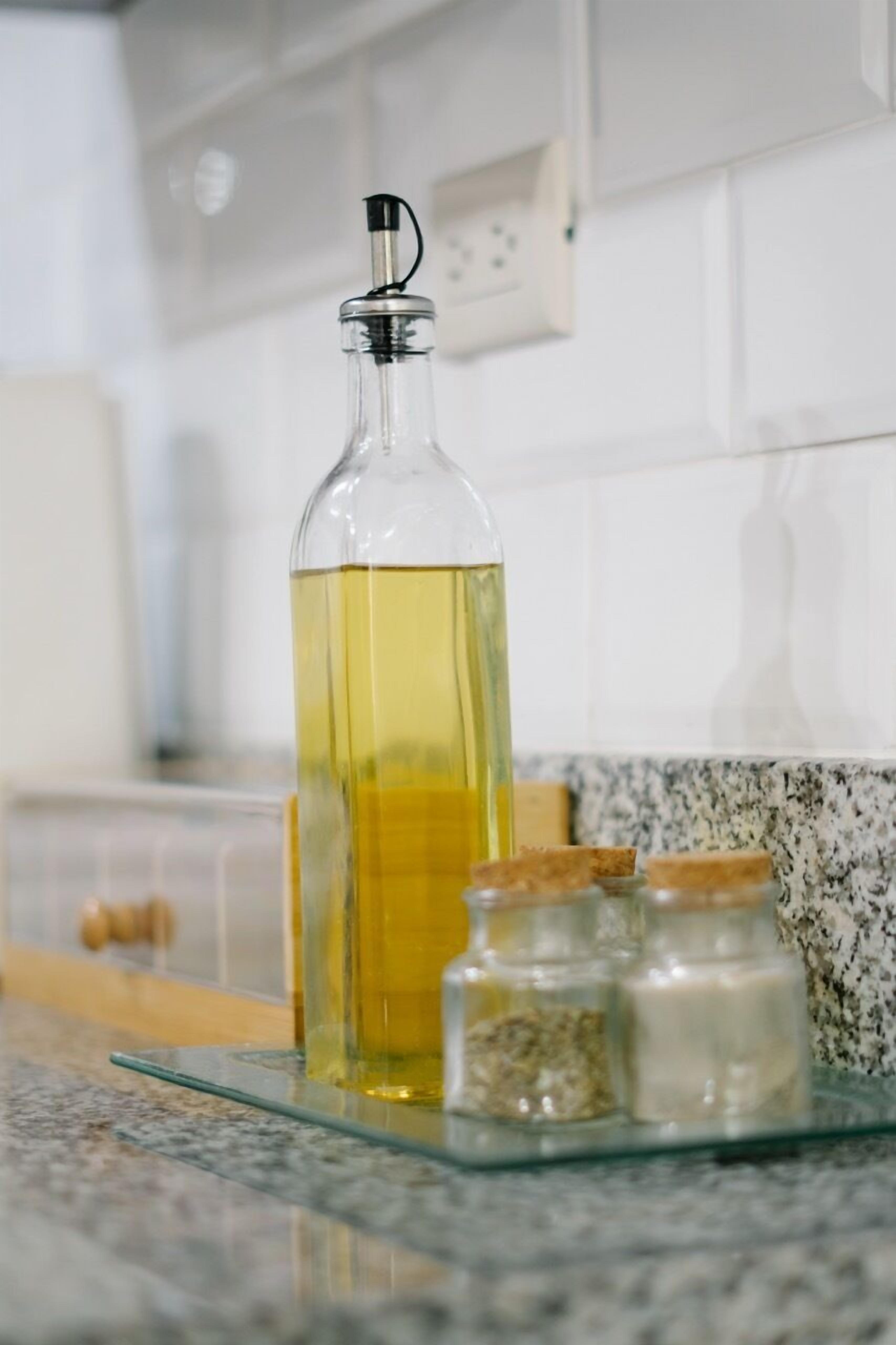 Una encimera de cocina con una botella de vidrio de líquido amarillo, posiblemente aceite, y dos pequeños frascos con tapas de corcho.