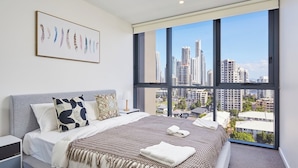 Un dormitorio moderno con una cama grande, vistas a la ciudad y una obra de arte enmarcada en la pared.