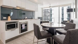 A modern kitchen with white cabinets, a gas stove, and a built-in oven. There is a dining area with a round table and four chairs. - 2 Bedroom Apartment with Parking, Pool, Gym (Fortitude Valley)