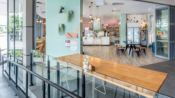 A modern cafe with a wooden table and chairs, a counter with a menu, and a refrigerator. - 2 Bedroom Apartment with Parking, Pool, Gym (Fortitude Valley)