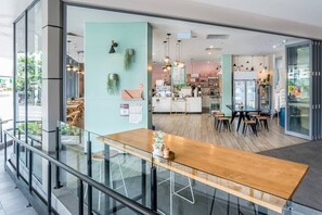 A modern cafe with a wooden table and chairs, a counter with a menu, and a refrigerator.