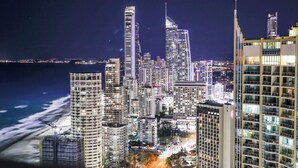 A nighttime cityscape with high-rise buildings, a beach, and a view of the ocean.