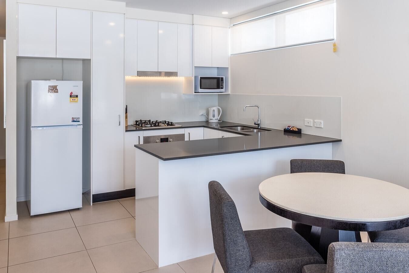 A modern kitchen with white cabinets, a built-in microwave, a gas stove, and a round dining table with grey chairs.