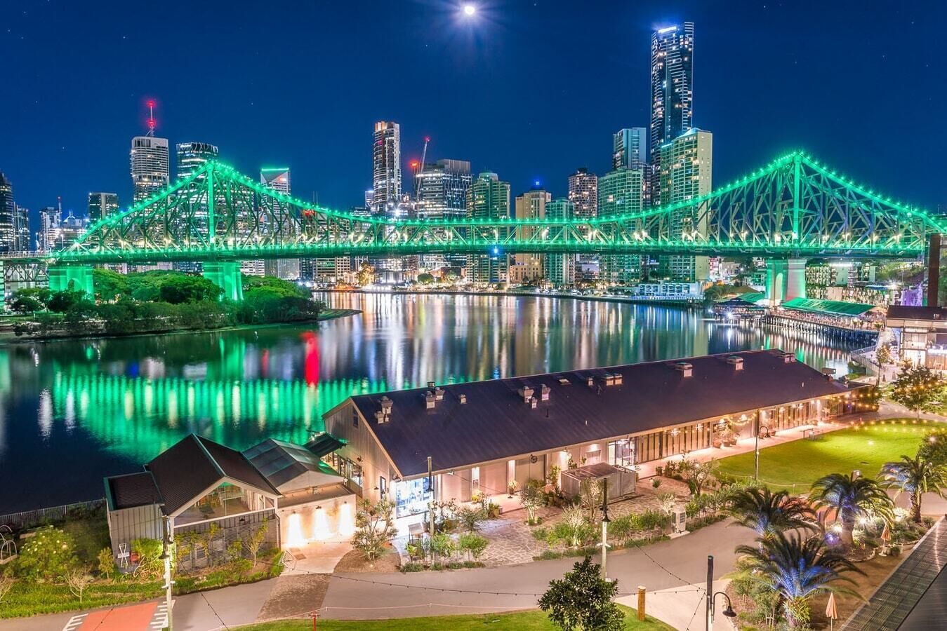 A cityscape with a prominent green-lit bridge over a river, reflecting city lights.