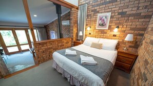 Een slaapkamer met een bakstenen muur, een bed met witte lakens, een nachtkastje en een raam met gordijnen.