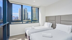 Ein modernes Hotelzimmer mit zwei Betten, einem großen Fenster mit Blick auf die Stadt und einer neutralen Farbgestaltung.