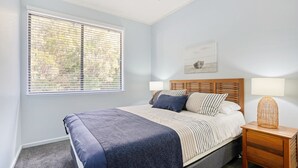 A bedroom with a bed, two bedside lamps, a nightstand, and a window with blinds. - Baden 58 - Rainbow Shores. Pools, outdoor spa, walk to beach. Tennis court (Rainbow Beach)