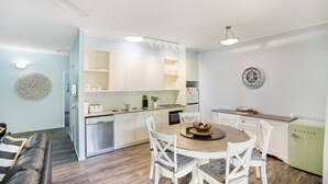 A modern kitchen with white cabinets, a dining table with chairs, and a refrigerator. - Baden 58 - Rainbow Shores. Pools, outdoor spa, walk to beach. Tennis court (Rainbow Beach)