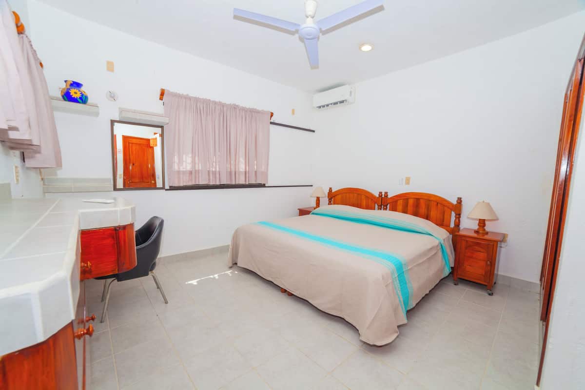 Une chambre à coucher comprenant un lit, un bureau, une chaise, un ventilateur de plafond et un appareil de climatisation.