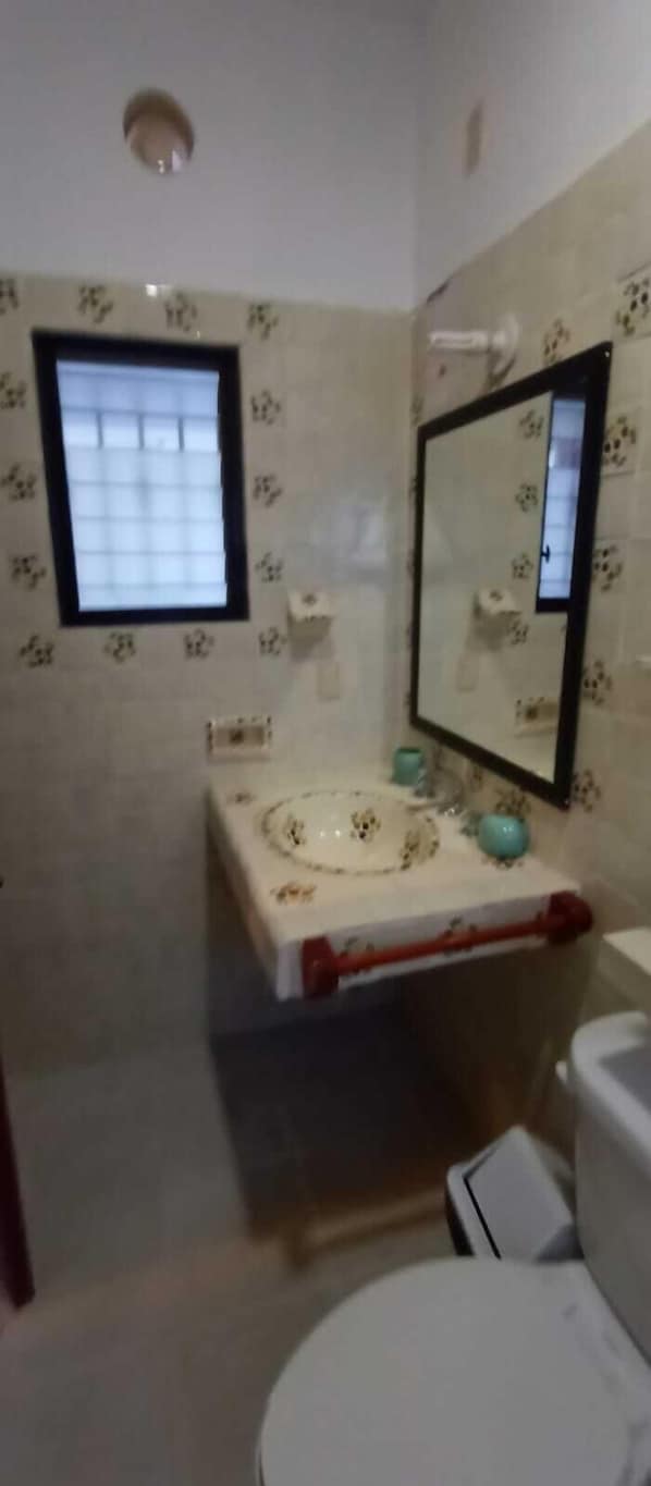Een kleine badkamer met toilet, een wastafel met spiegel erboven en een raam met zonwering.