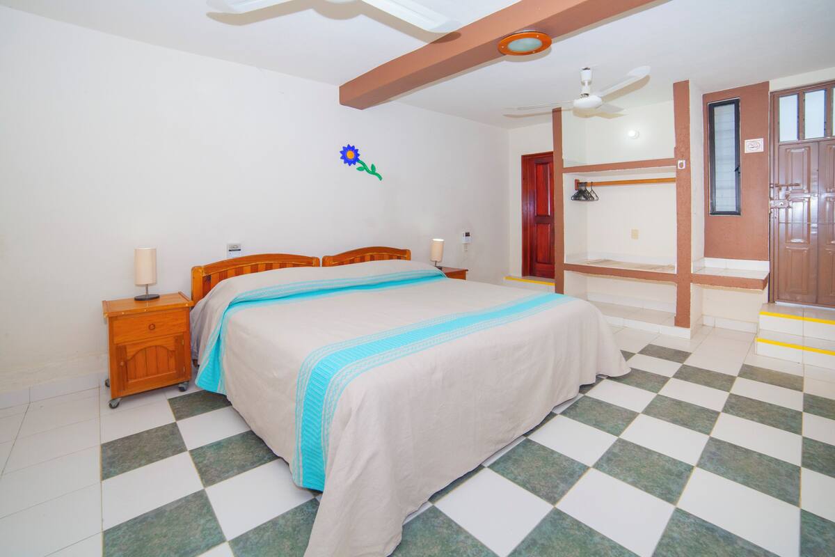 Une chambre à coucher avec un lit, des tables de chevet, un ventilateur de plafond, un élément décoratif mural et un sol à carreaux.