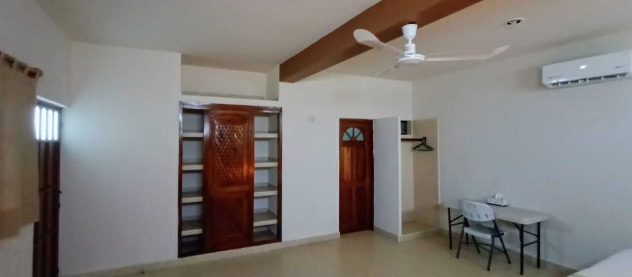 Una stanza con ventilatore a soffitto, un tavolo bianco con sedie, una porta di legno e un condizionatore d'aria bianco.